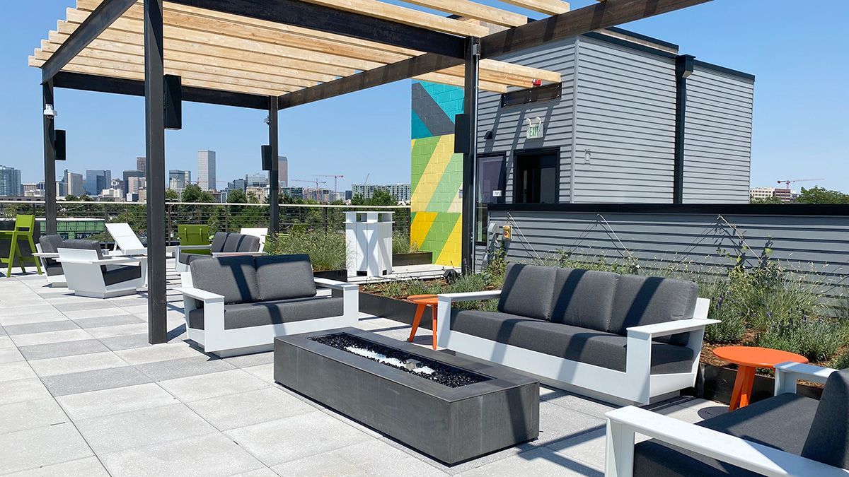 Rooftop patio with seating, fire pit, and city skyline view on a sunny day.
