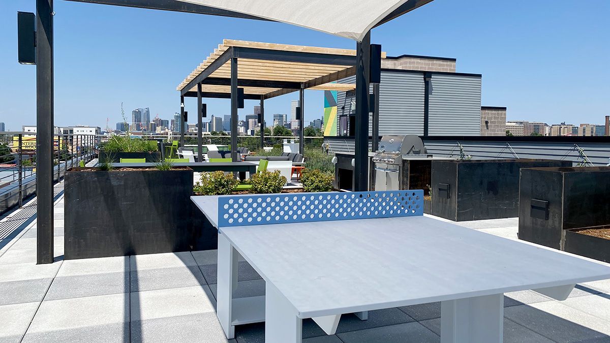 Rooftop ping pong table with cityscape background under a shaded pergola on a sunny day.
