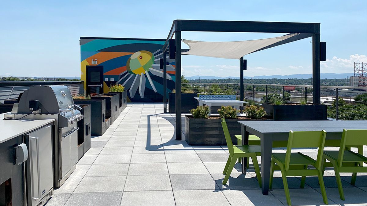 Rooftop deck with grills, table, chairs, and pergola with sunshade. Mural on the wall. Overlooking city.