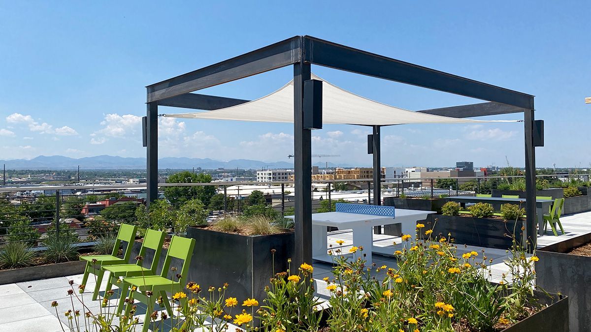 Rooftop patio with pergola, seating, tables, and city view under a clear, blue sky.
