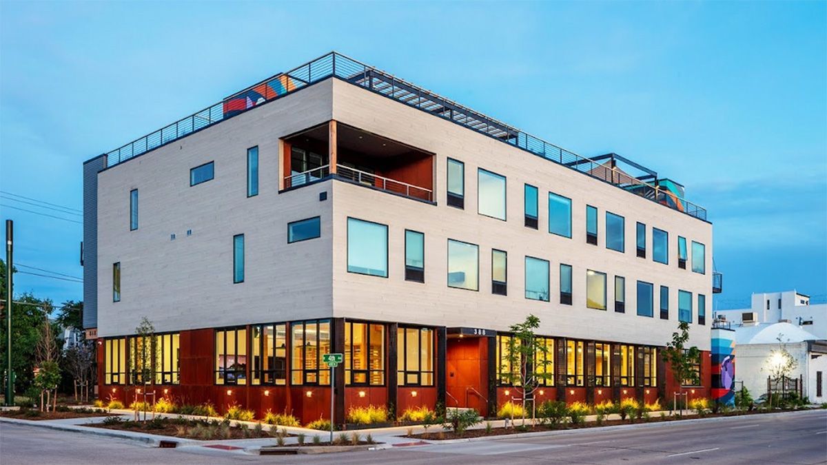 Modern, multi-story building with a flat roof and numerous windows. Exterior painted white and brown.