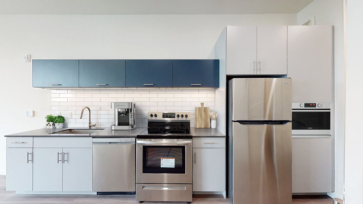 Modern kitchen with stainless steel appliances, white and blue cabinets, and a gray countertop.