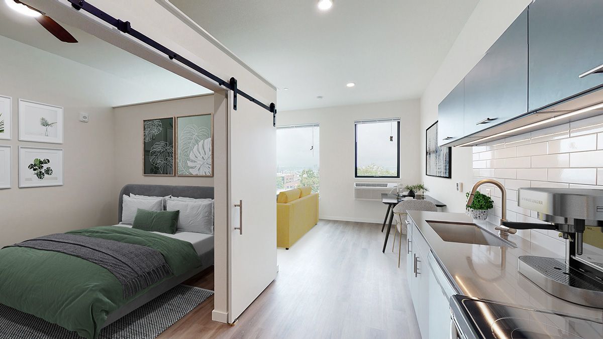 Small apartment with a bedroom, kitchen, and living area. The bed has green bedding. A sliding door separates the bedroom.