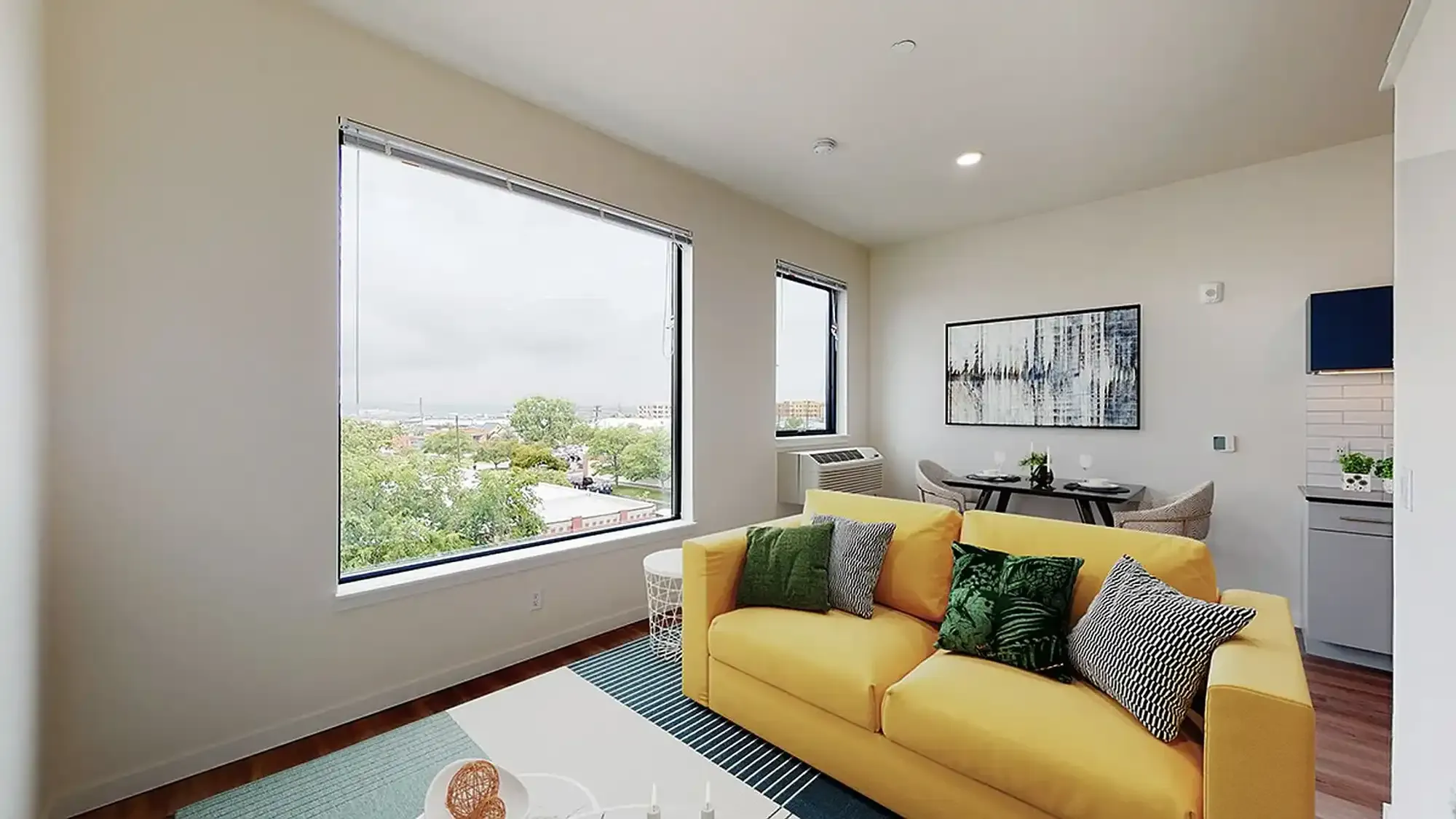 Yellow couch in a modern living room with a large window overlooking a cityscape.