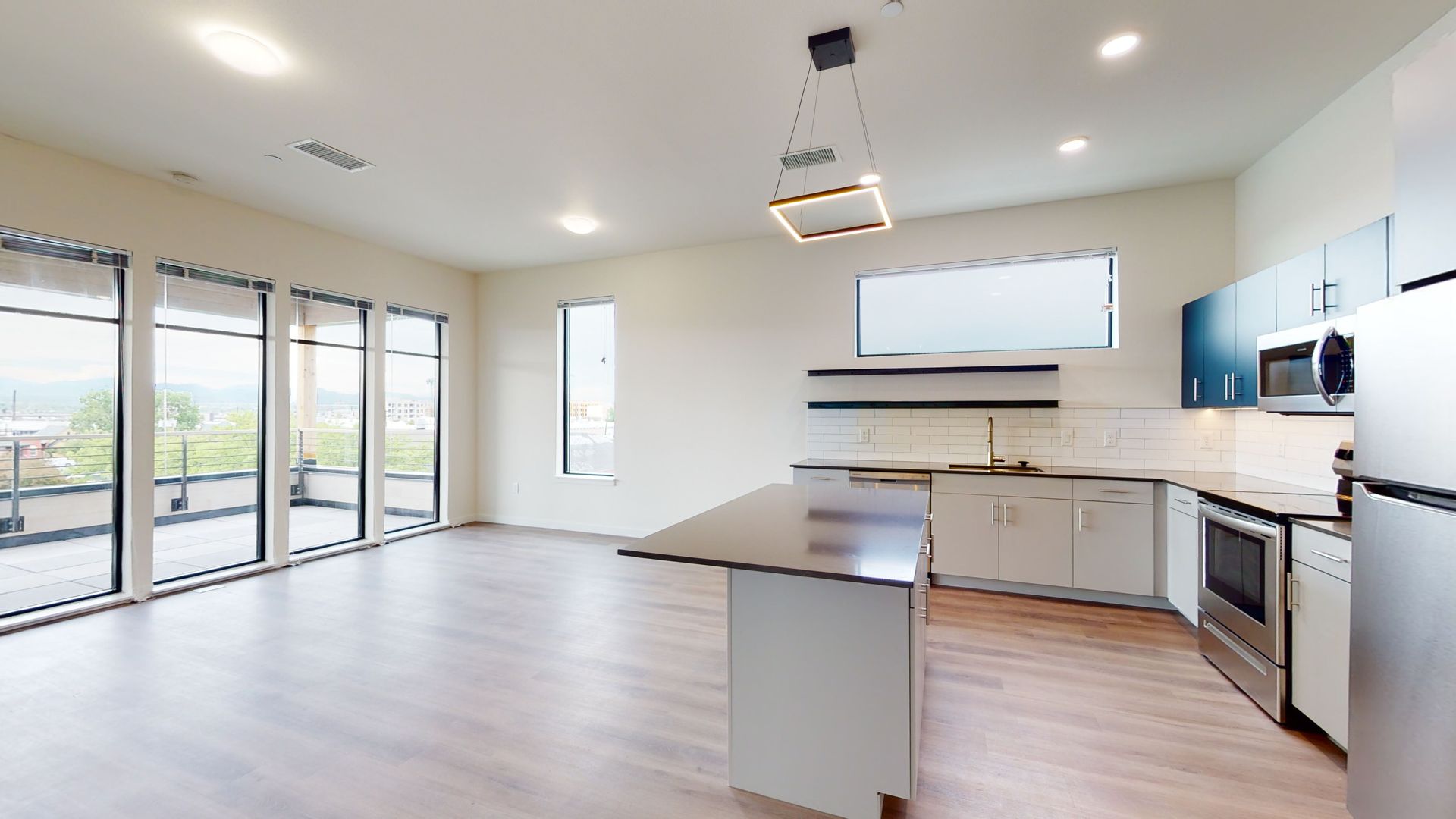 Spacious modern apartment: light wood floors, white walls, stainless steel appliances, and large windows.