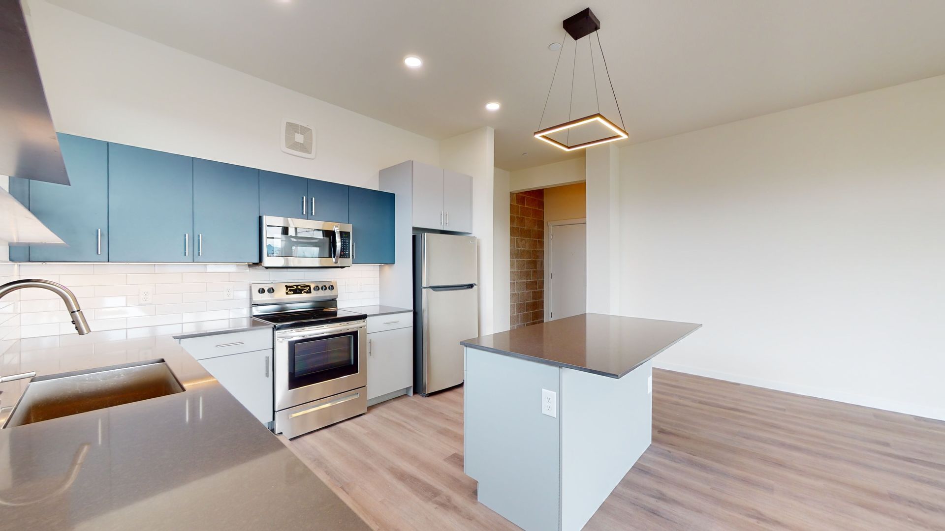 Modern kitchen with blue upper cabinets, stainless steel appliances, and island.