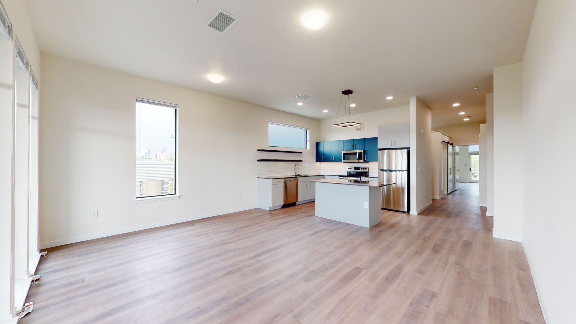 Open-concept living space with kitchen. Light wood floors, white walls, stainless steel appliances, and a modern design.
