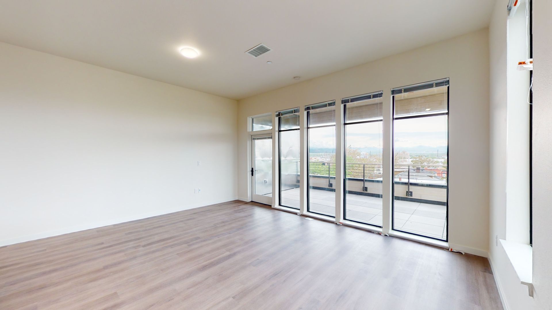 Empty room with large windows, light wood floor, and white walls.