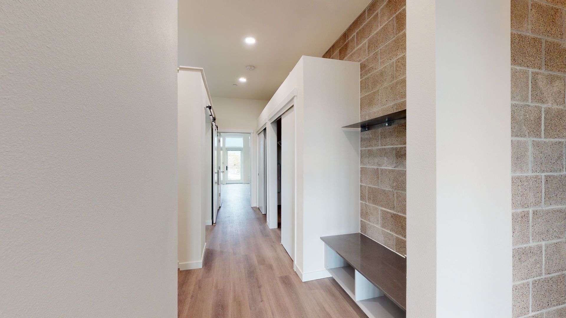 Hallway with wooden floor, white walls and storage, and exposed brick accent wall.