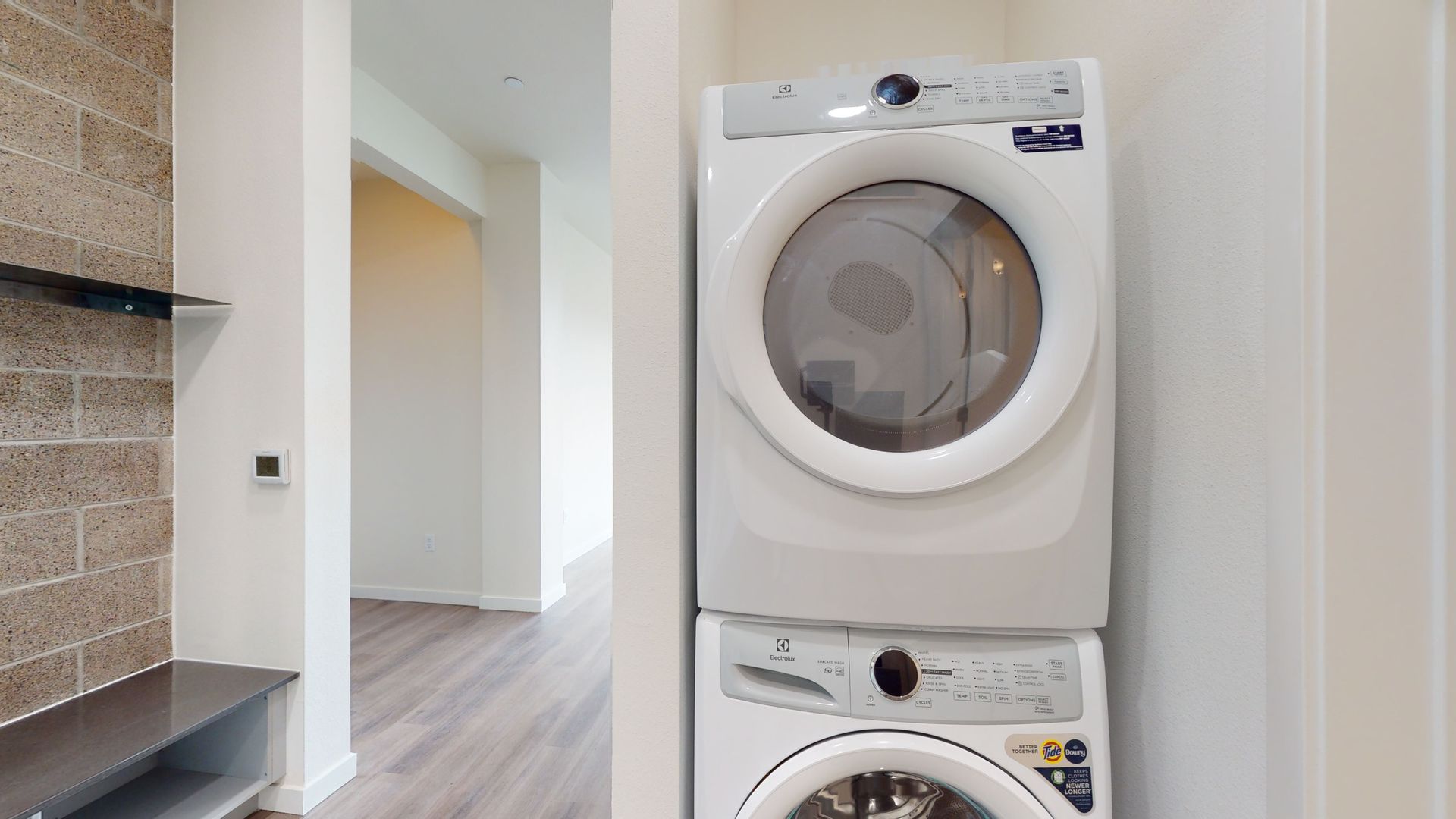 Stacked white washer and dryer in a laundry room, adjacent to an entrance to another room.
