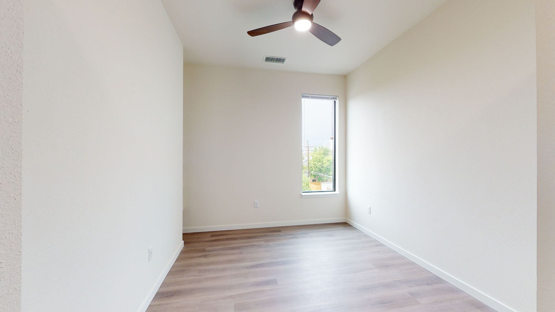 Empty room with wood-look flooring, a ceiling fan, and a tall, narrow window.