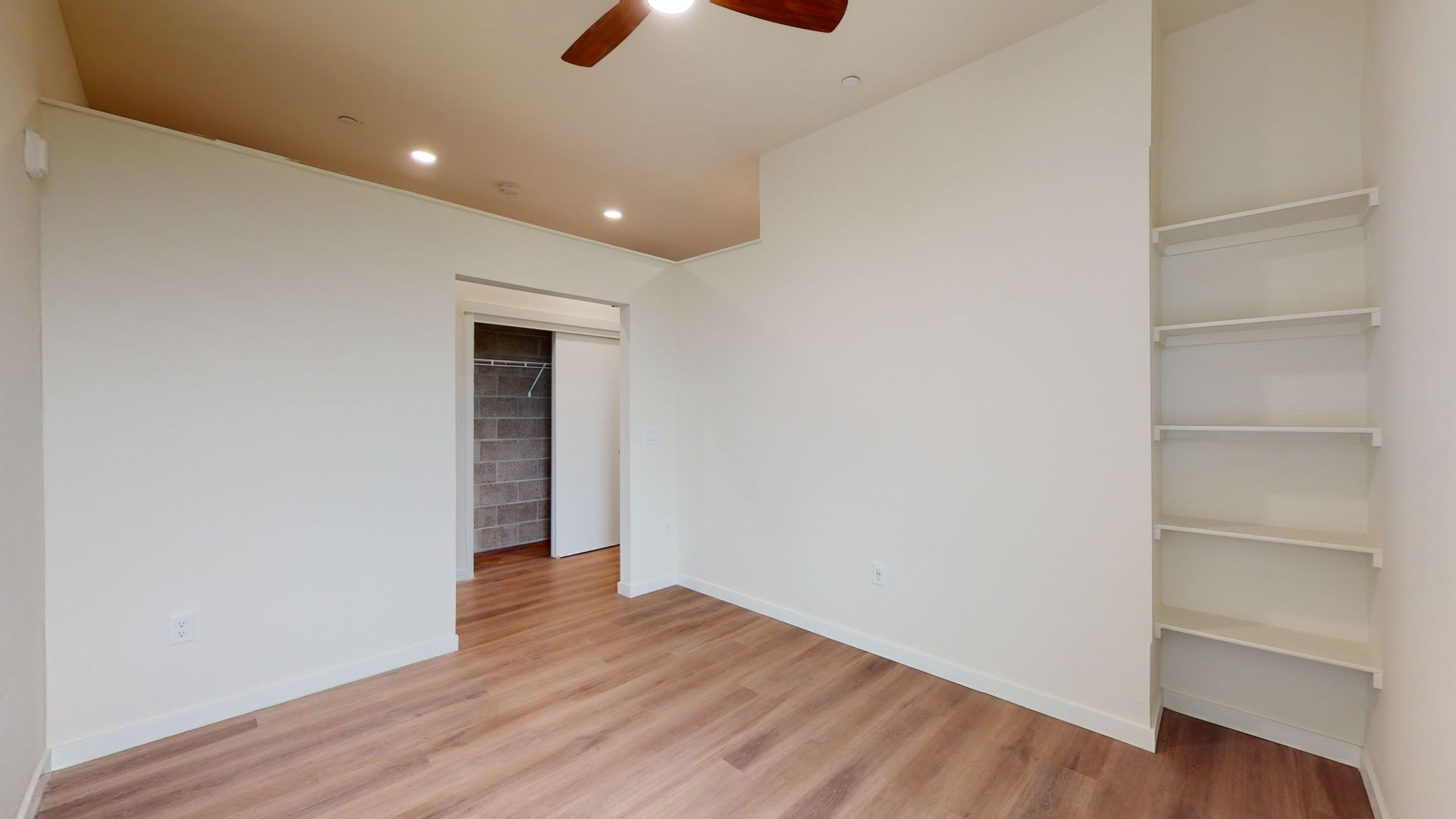 Empty room with wooden floors, white walls, built-in shelving, and a doorway.