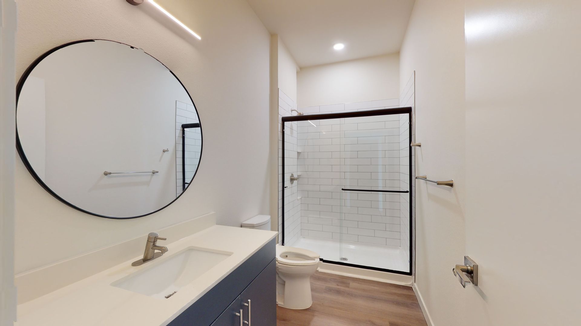 Bathroom with a round mirror, blue vanity, white countertop, and glass shower.