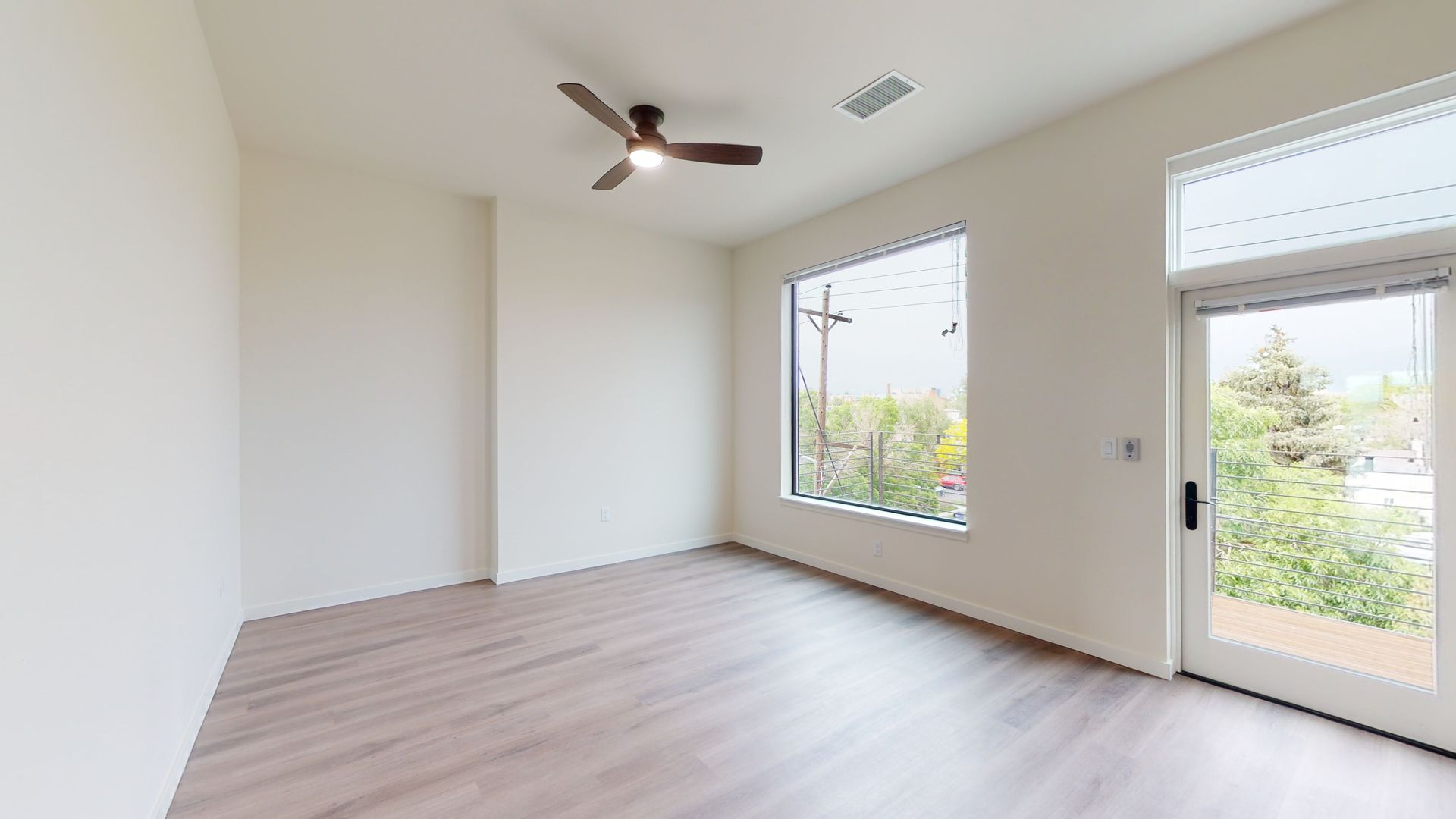 Empty room with wood floors, large window, and door. Ceiling fan and white walls.