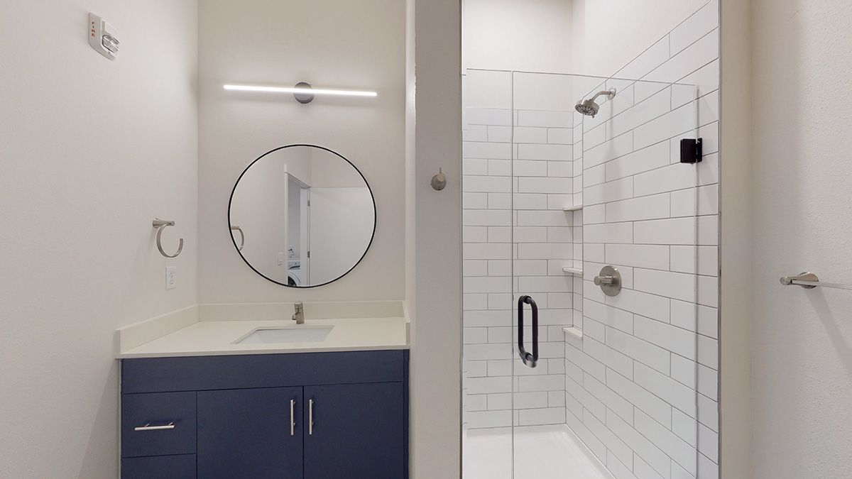 Modern bathroom with blue vanity, round mirror, and glass shower.