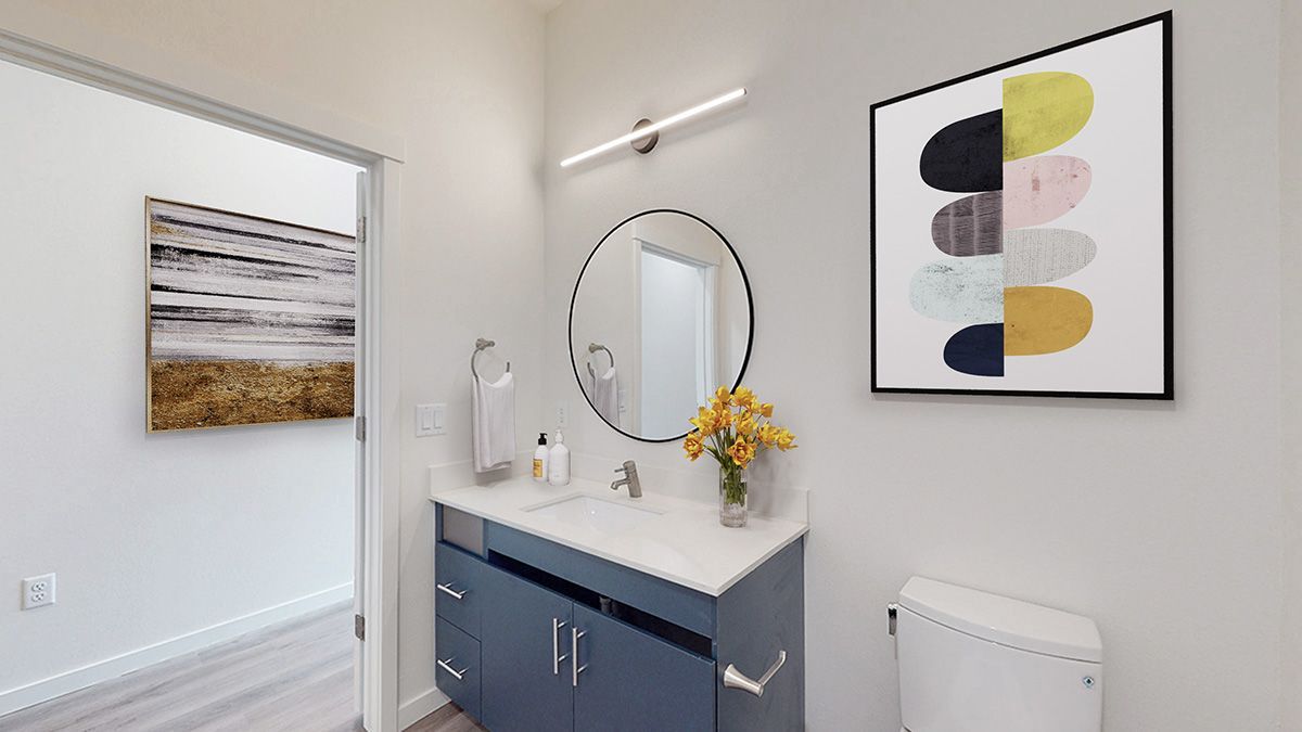 Modern bathroom with blue vanity, round mirror, abstract art, and a bouquet of yellow flowers.
