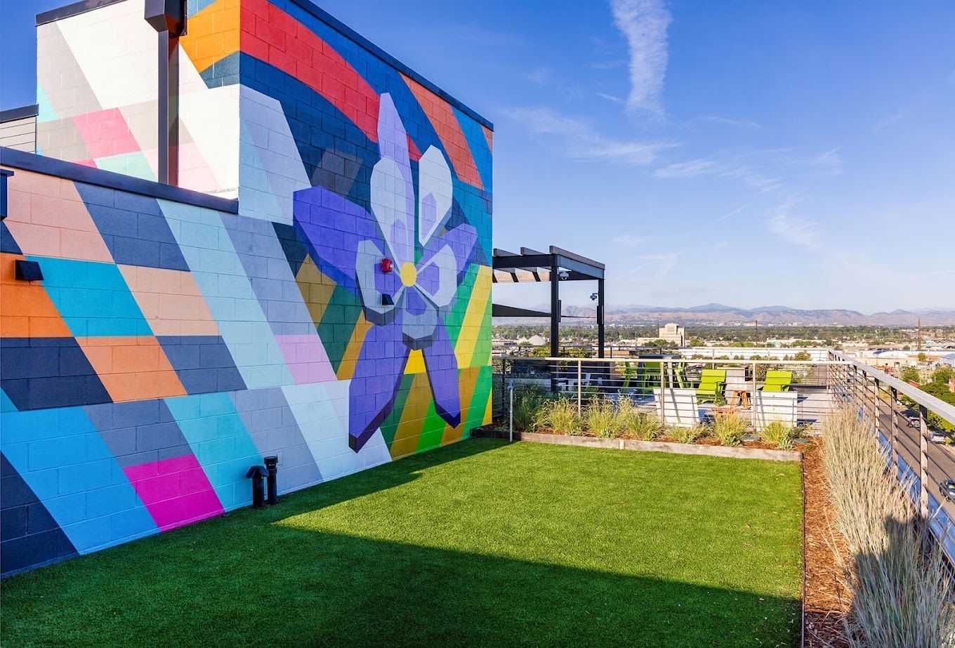 Rooftop patio with colorful mural, artificial grass, and city views on a sunny day.