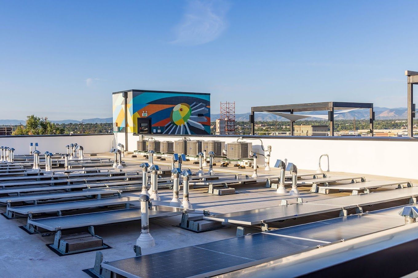Rooftop view of solar panels, with a colorful mural and HVAC units, under a clear, blue sky.
