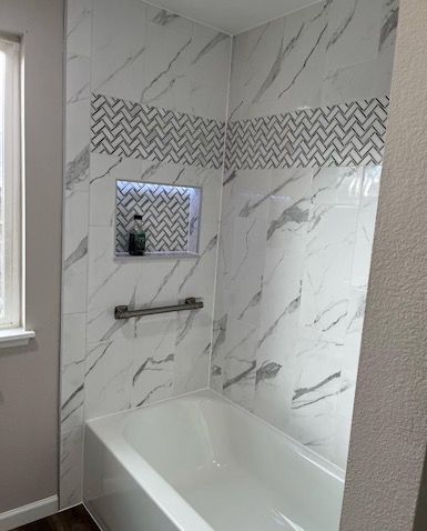 A bathtub in a bathroom with marble tiles and a window.