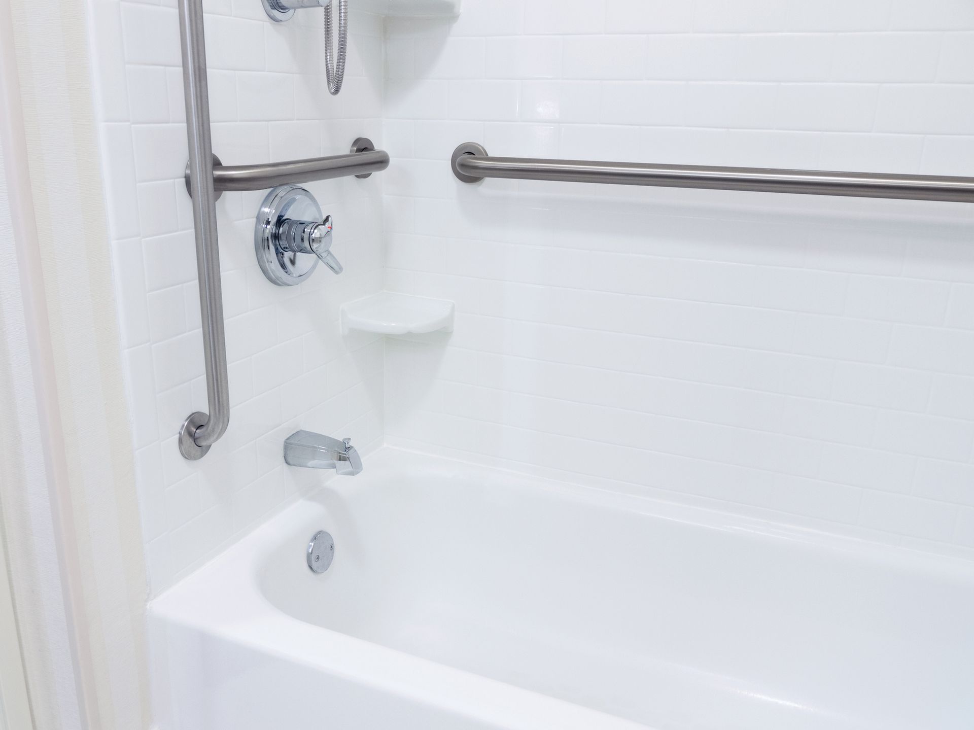 A white bathtub with stainless steel handles in a bathroom.