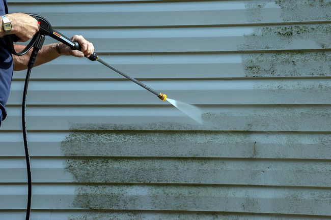 A man is cleaning the side of a house with a high pressure washer.