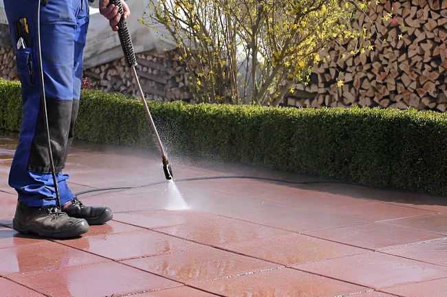 A man is using a high pressure washer to clean a patio.