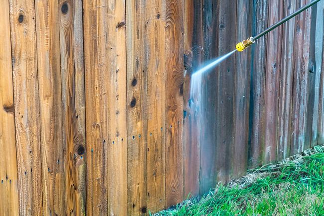 A person is using a high pressure washer to clean a wooden fence.