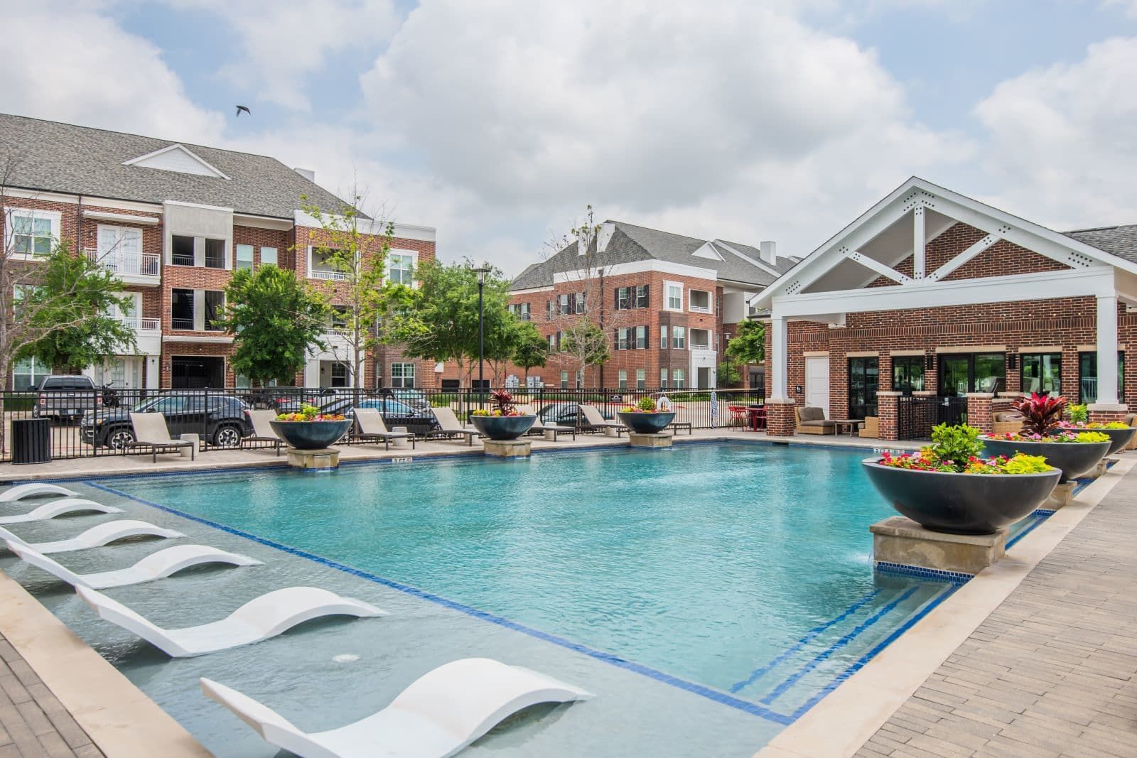 Outdoor community pool with lounge chairs and planters at an apartment complex.