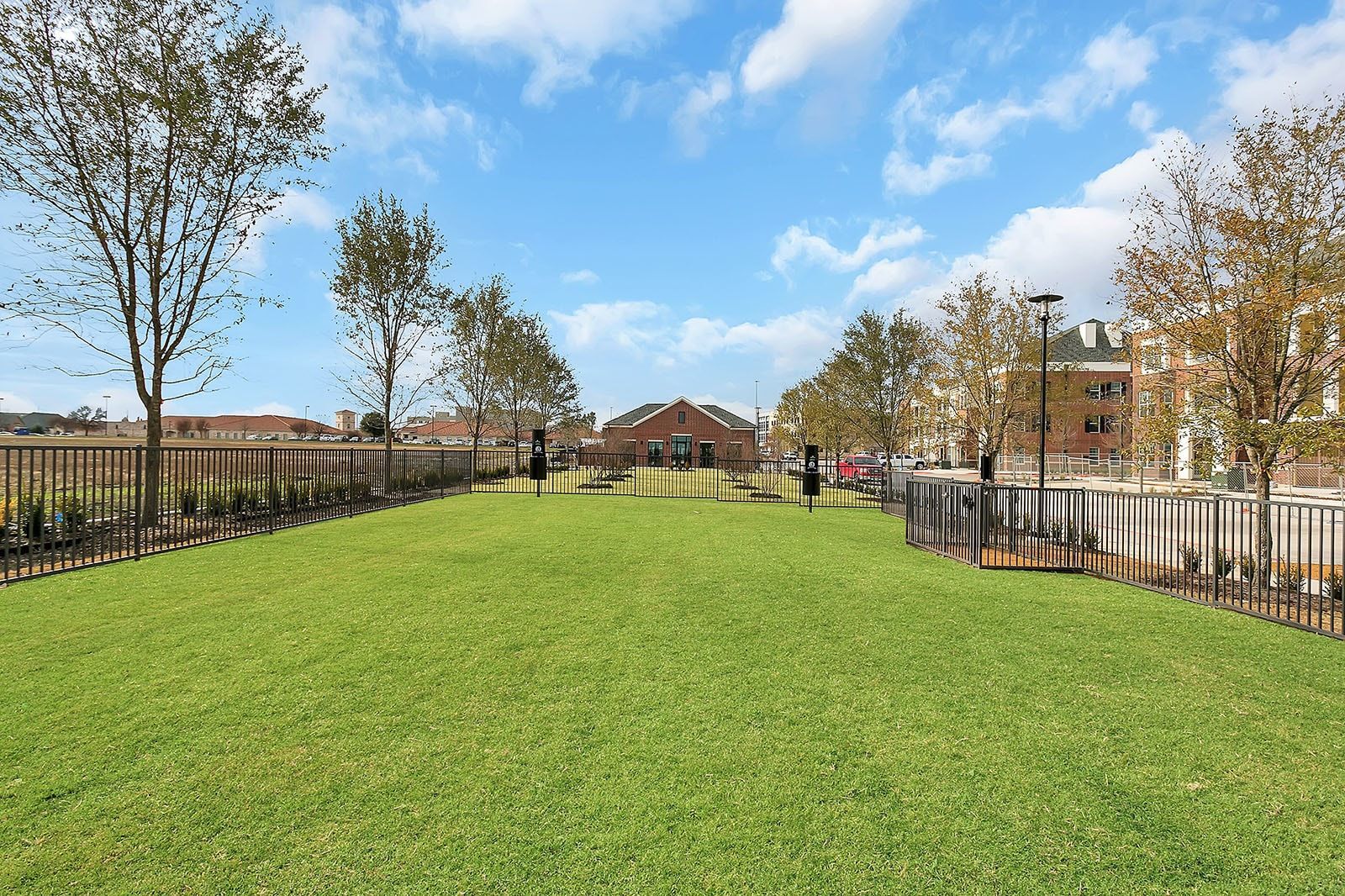 Open grassy communal courtyard with trees, fencing, and a brick building in the background.