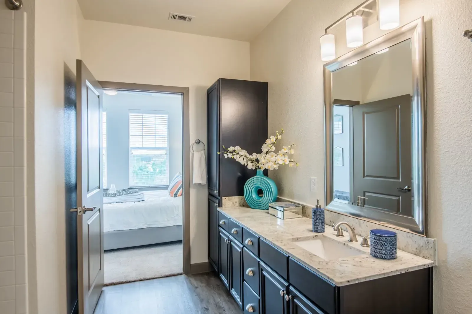 Bathroom with dark wood vanity, marble countertop, large mirror, and doorway to a bedroom.