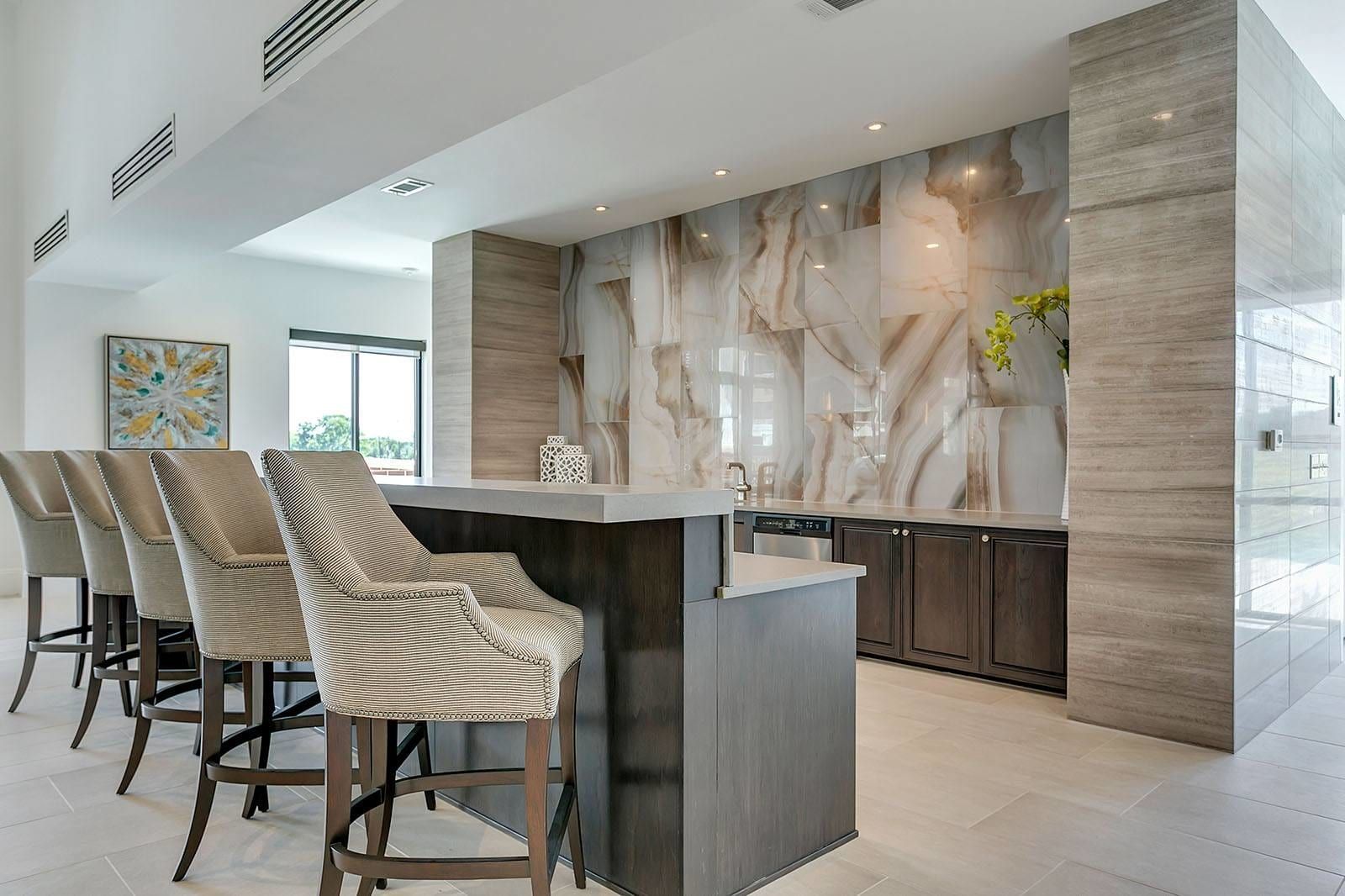 Modern communal kitchen with marble backsplash, dark cabinetry, and upholstered bar stools.