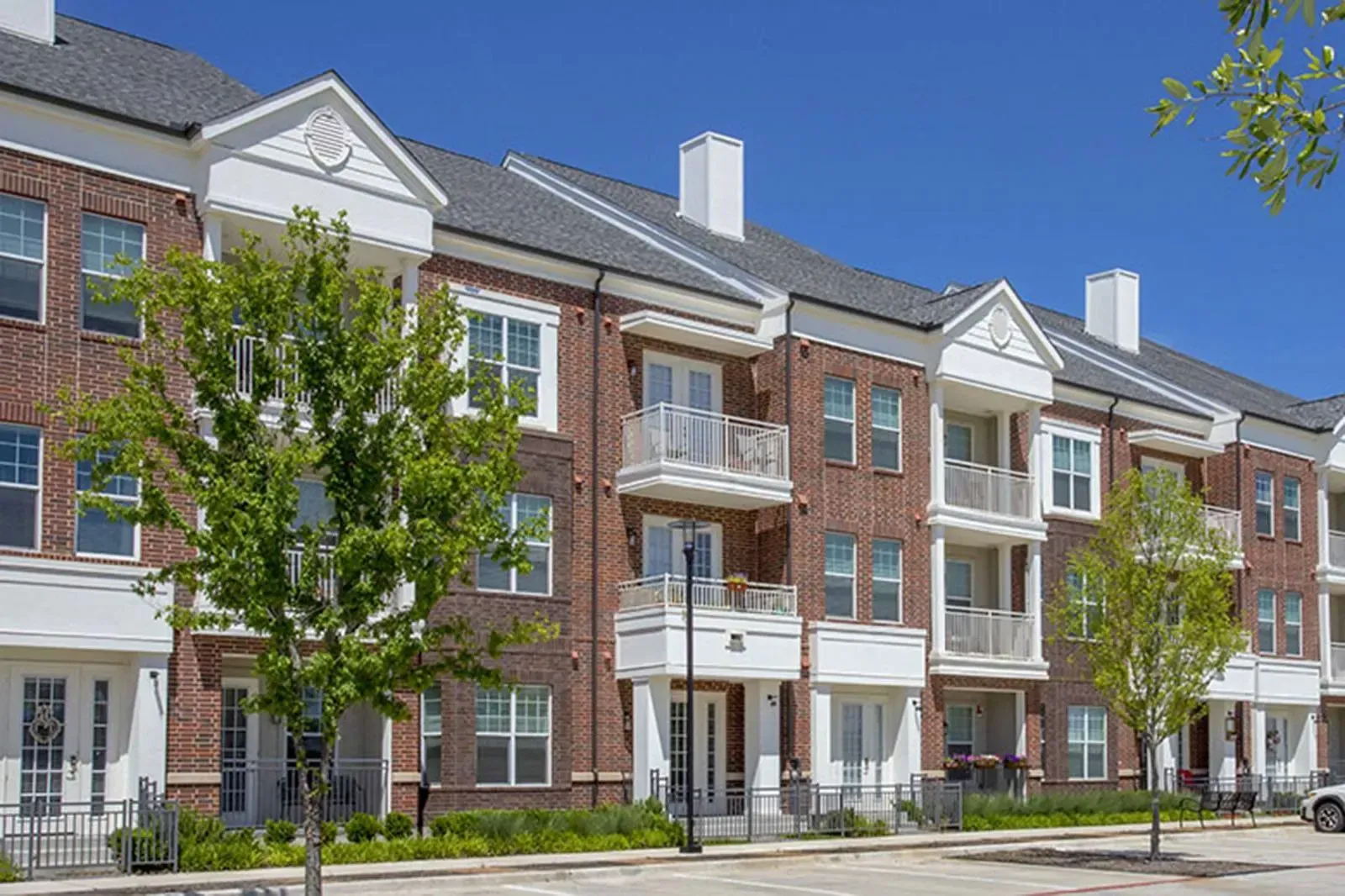 Exterior view of a brick apartment building with balconies and trees along the sidewalk.