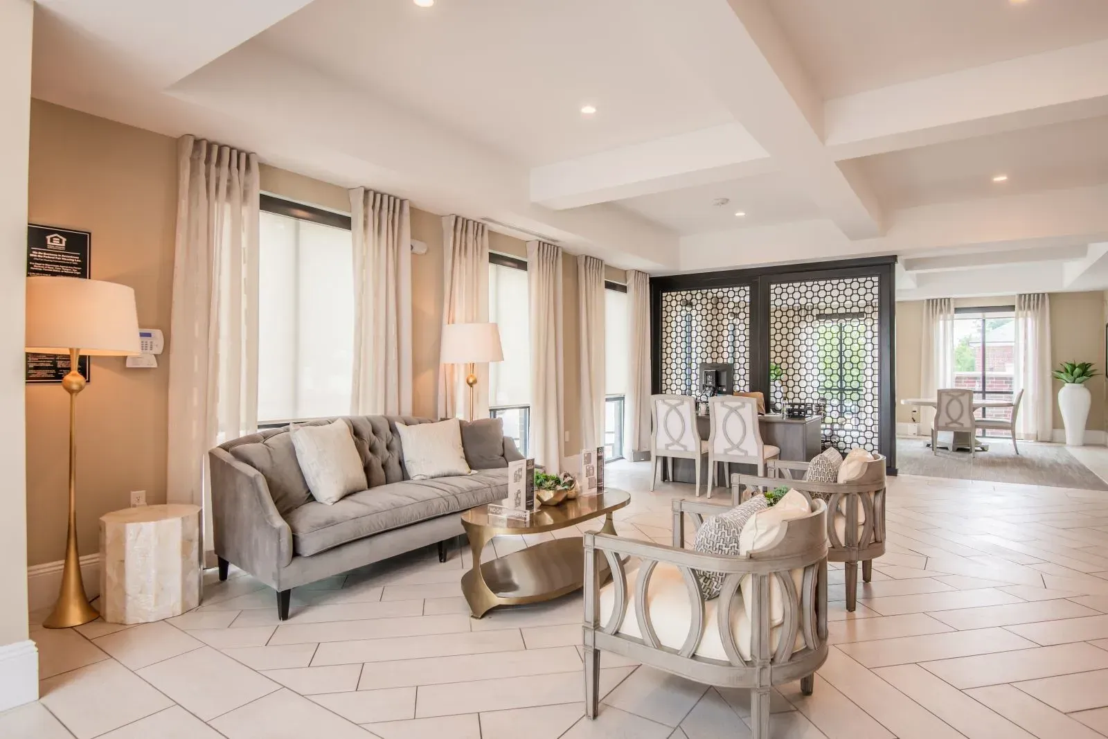 Bright residential lobby lounge with beige walls, white curtains, and seating.