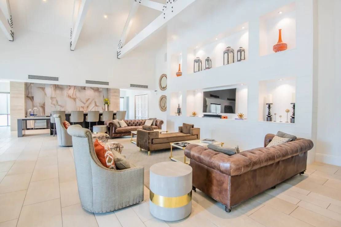 Bright modern living room with white walls, beige tile floor, and brown leather sectional sofas