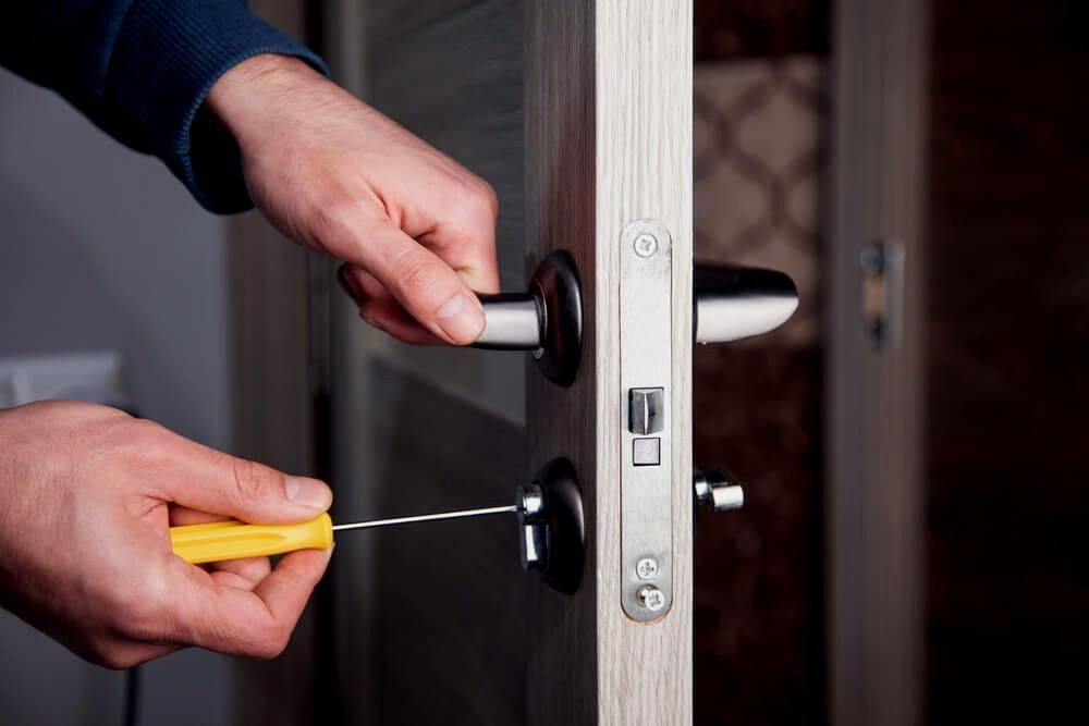 A Man Is Fixing A Door Handle With A Screwdriver — Troy Cummings Locksmith In Cooktown, QLD