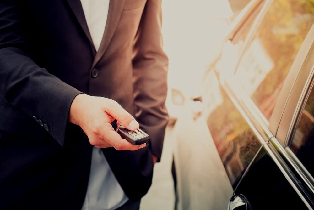 A Man In A Suit Is Holding A Remote Control In Front Of A Car — Troy Cummings Locksmith In Innisfail, QLD