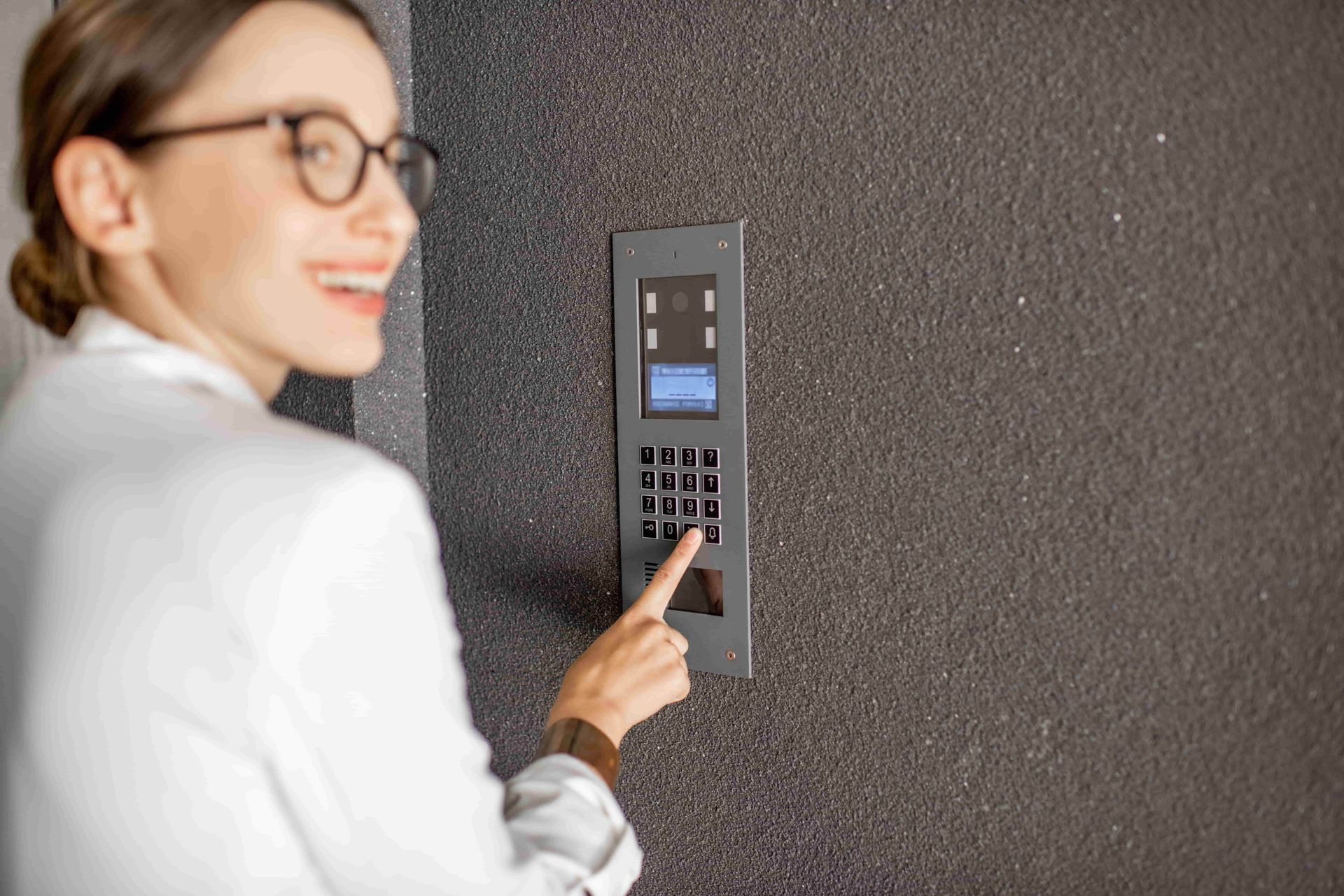 A Woman Wearing Glasses Is Pressing A Button On A Wall — Troy Cummings Locksmith In Tully, QLD