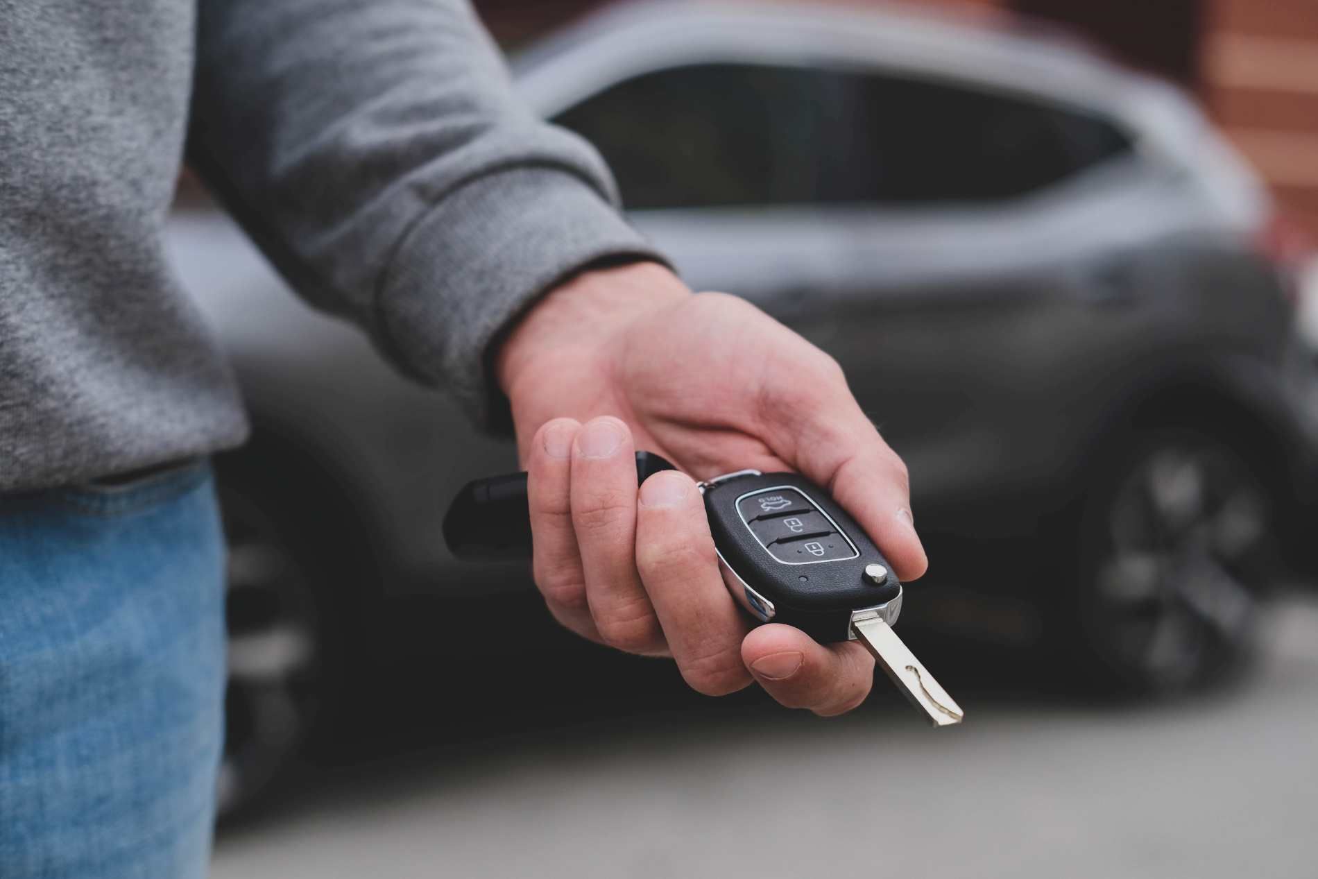 A Man Is Holding A Car Key In Front Of A Car — Troy Cummings Locksmith In Mornington Island, QLD
