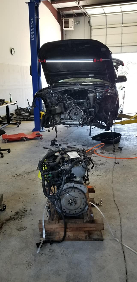 Car engine being worked on in a garage. The engine is out of the vehicle and being worked on.