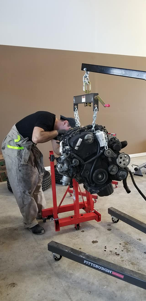 Mechanic working on an engine lifted by a crane. The engine sits on a red stand.