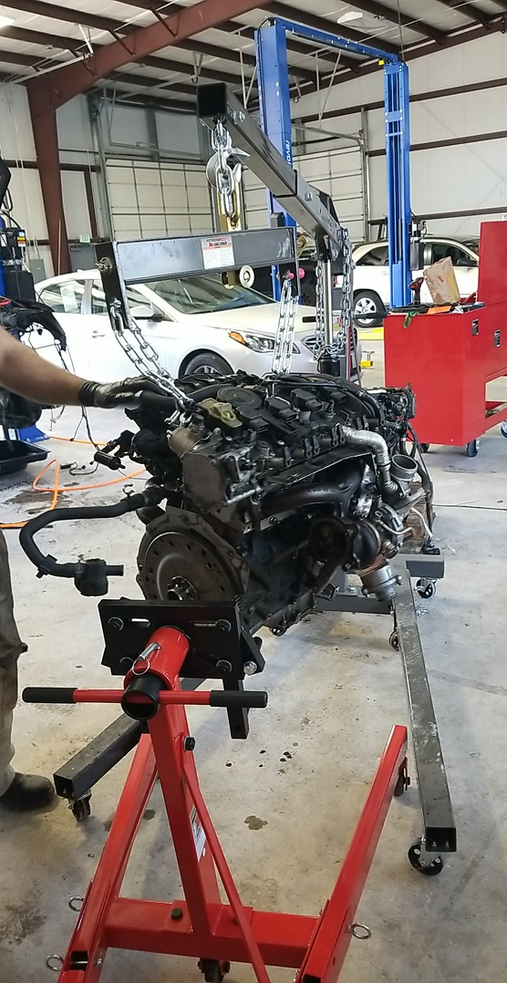 Engine being lifted in a repair shop; red lift, car, and two other lifts are present.