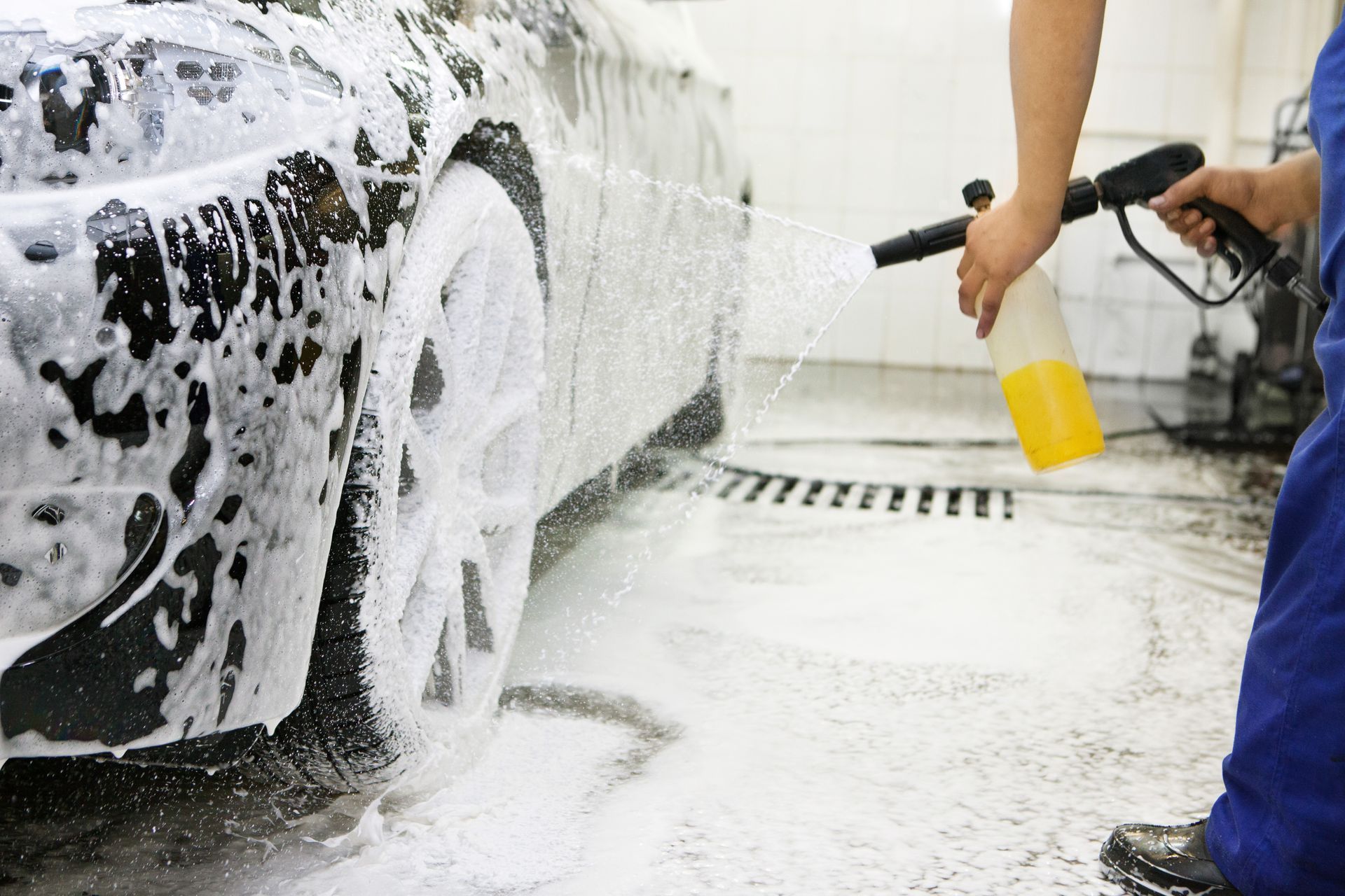 Person spraying foam on a black car wheel in a car wash bay.