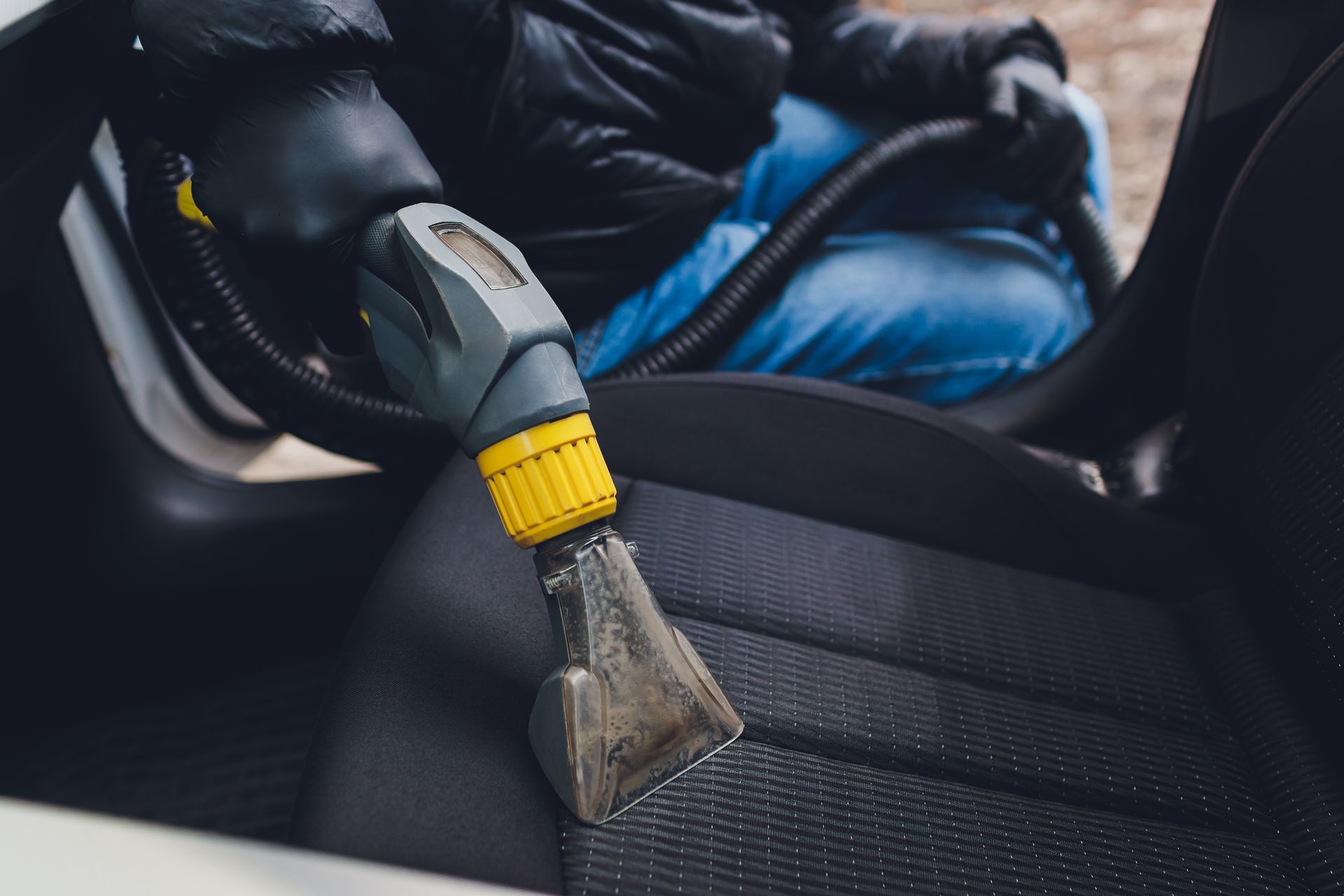 Person vacuuming a car seat with a handheld cleaning tool.