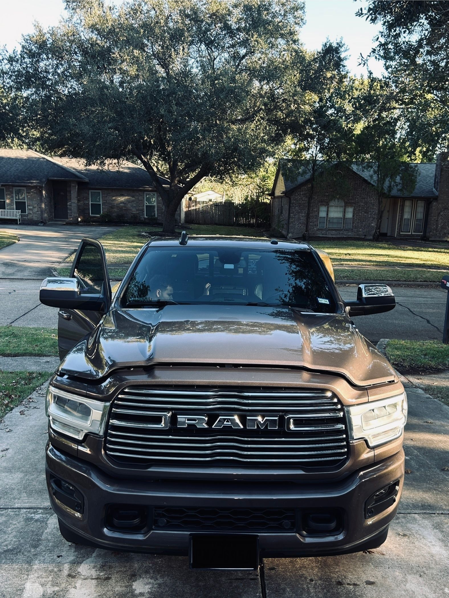 Brown RAM truck parked in a driveway in front of houses; open driver-side door.