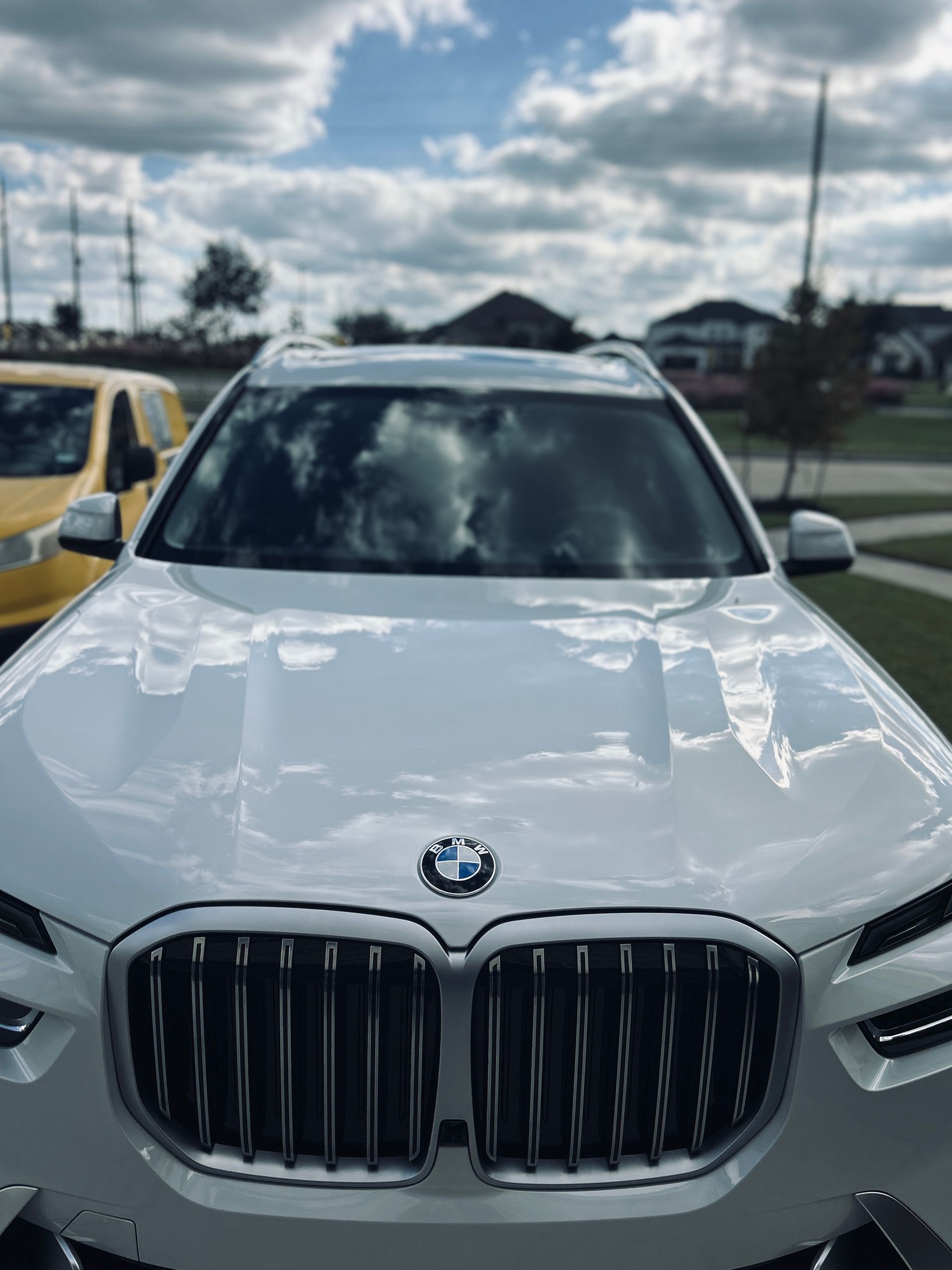 White BMW SUV with silver grille, parked outdoors on a sunny day with cloudy sky.