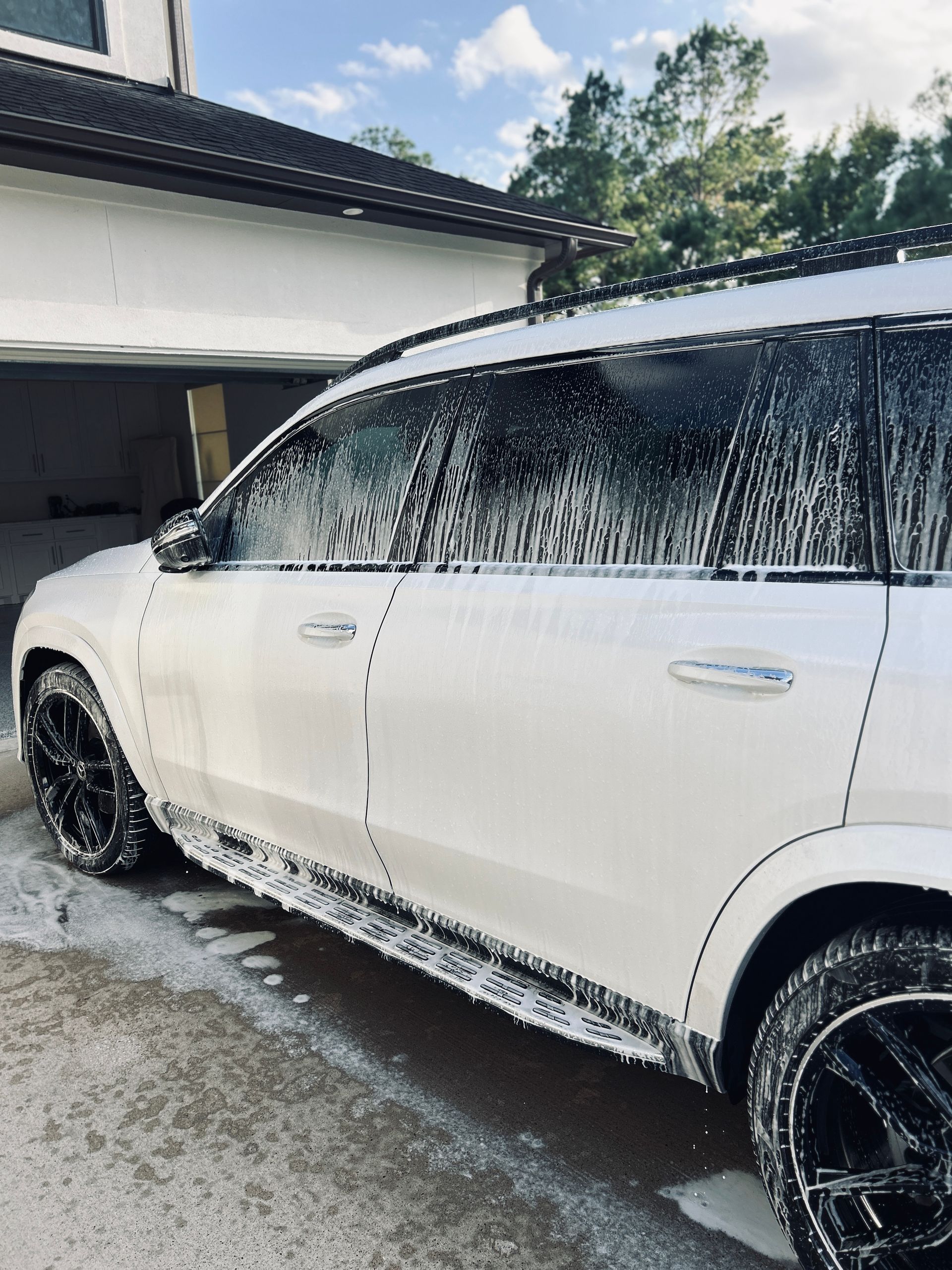 White SUV covered in soapy foam, parked near a garage.