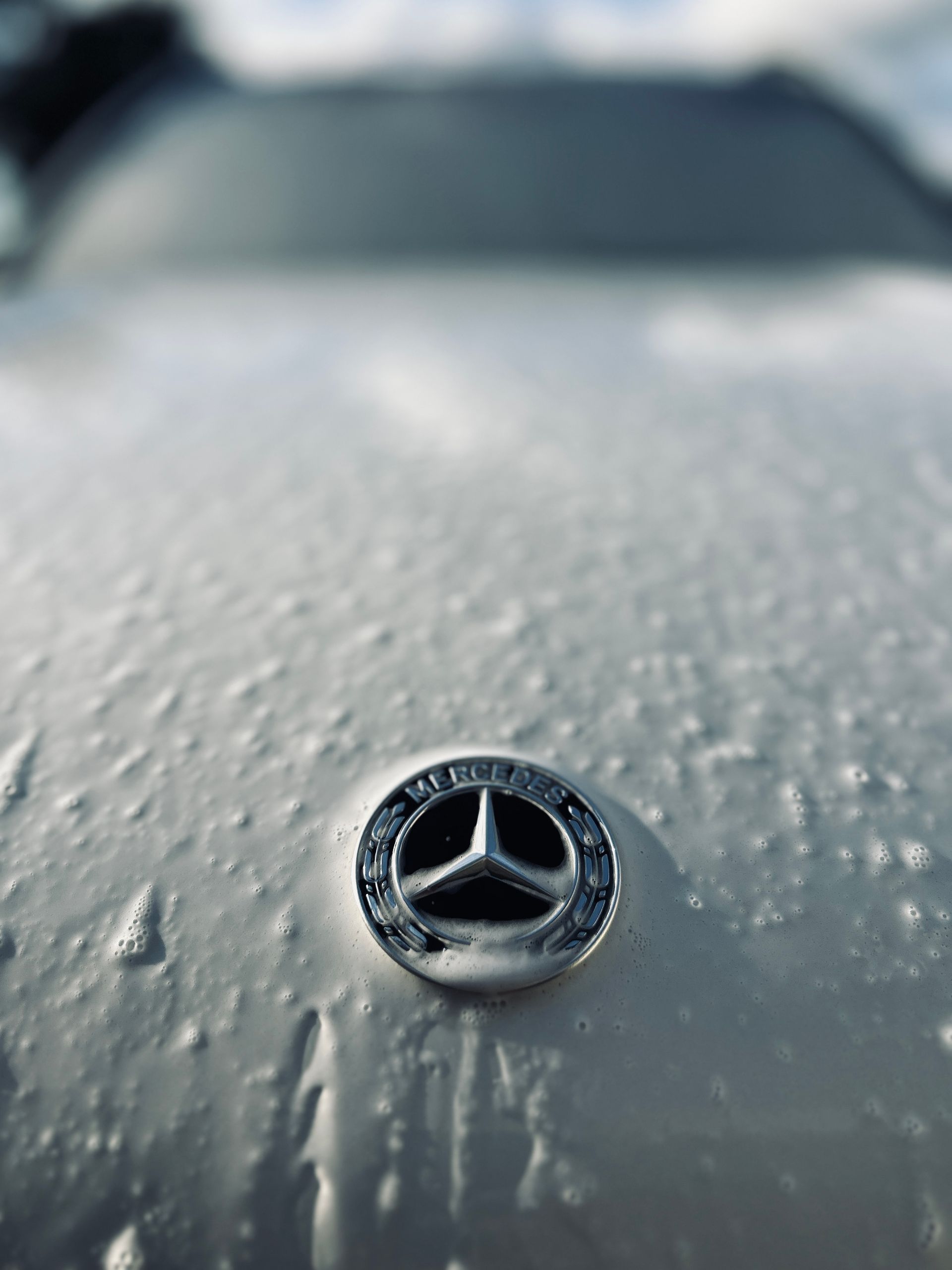 Mercedes-Benz emblem on a white car hood covered in soap suds.