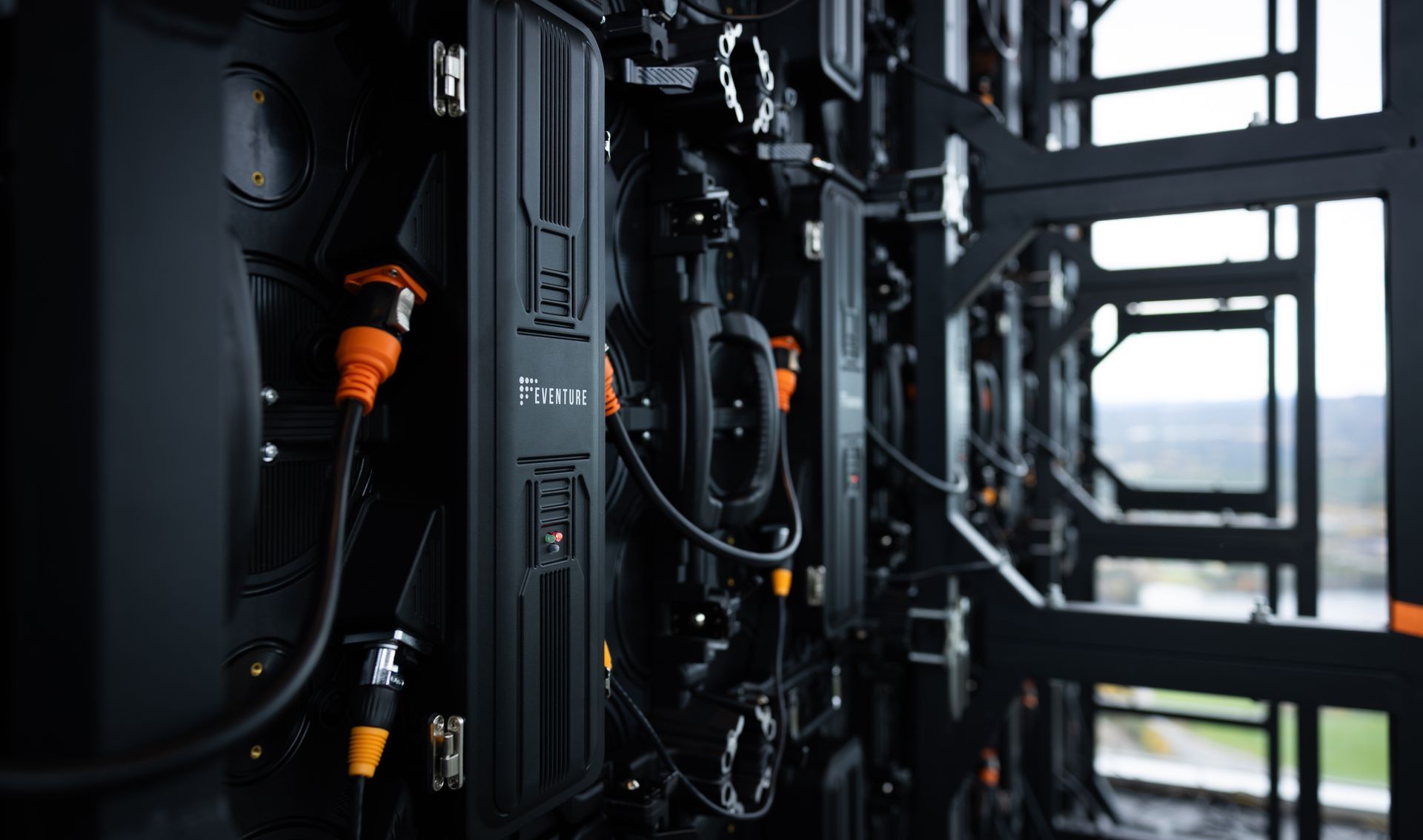 Nærbilde av et svart LED-videodisplaypanelsystem med diverse tilkoblede kabler og komponenter, utendørs.