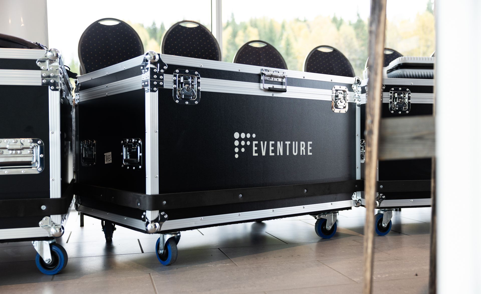 Svarte kofferter for eventutstyr med hjul, stablet innendørs, med «Eventure»-logoen.