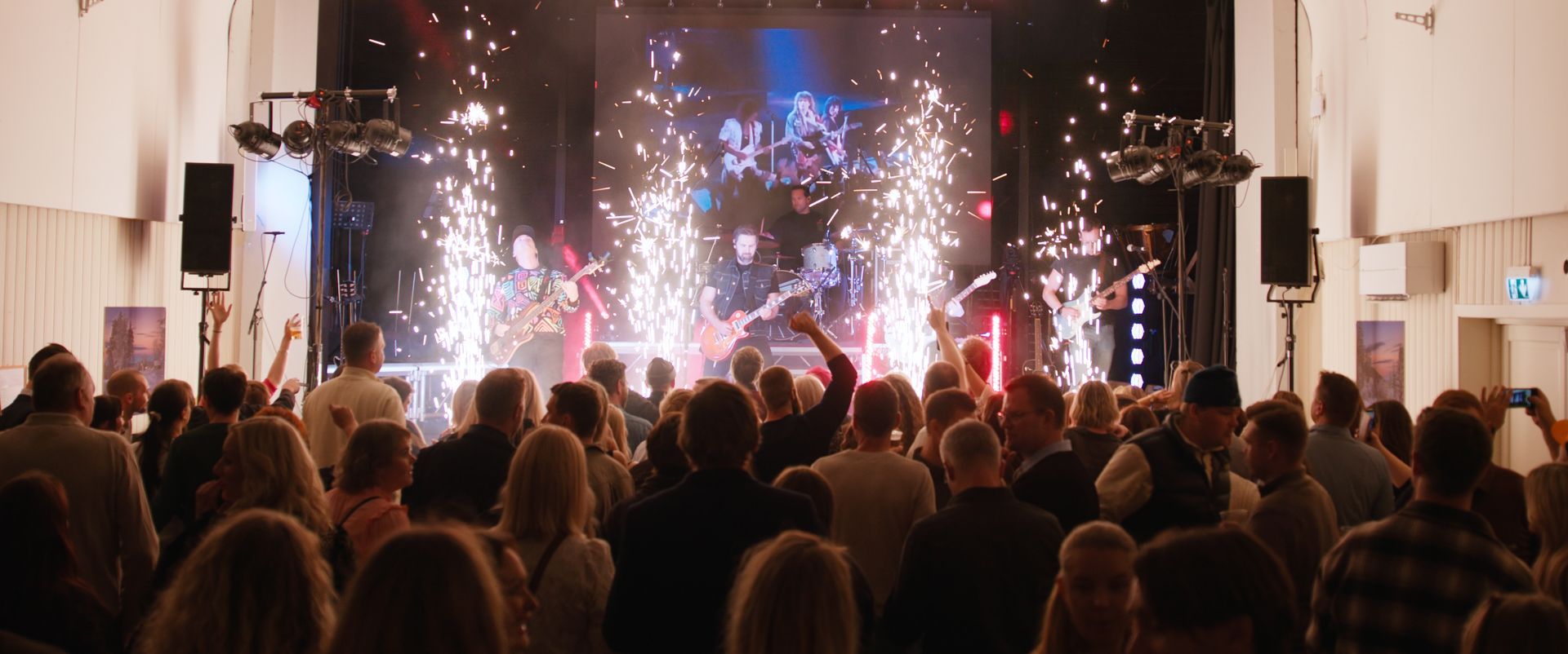 Et band opptrer på scenen med pyroteknikk mens et publikum jubler på et sted.